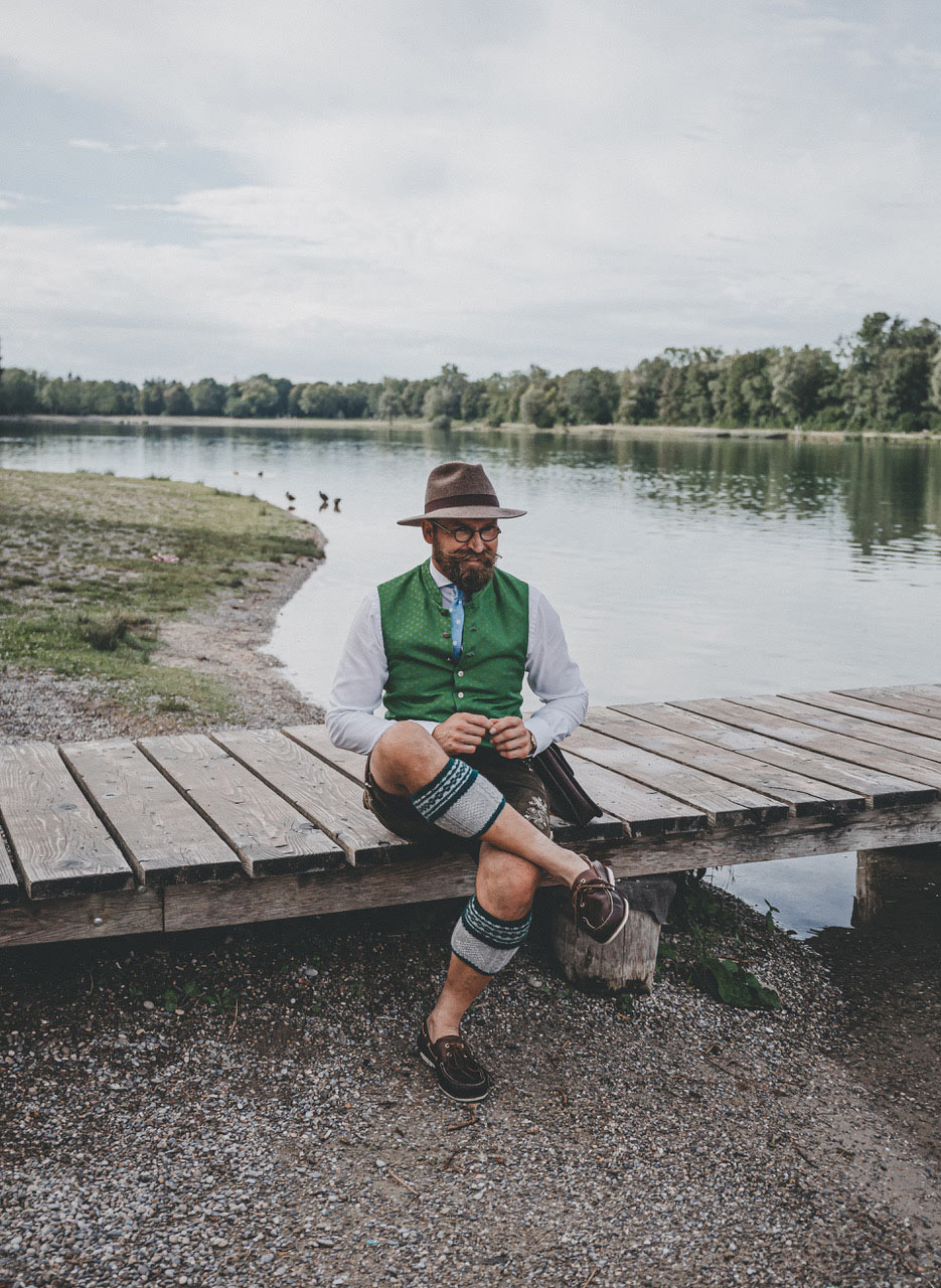 Albert wearing a hat and a green vest sitting next to a lake